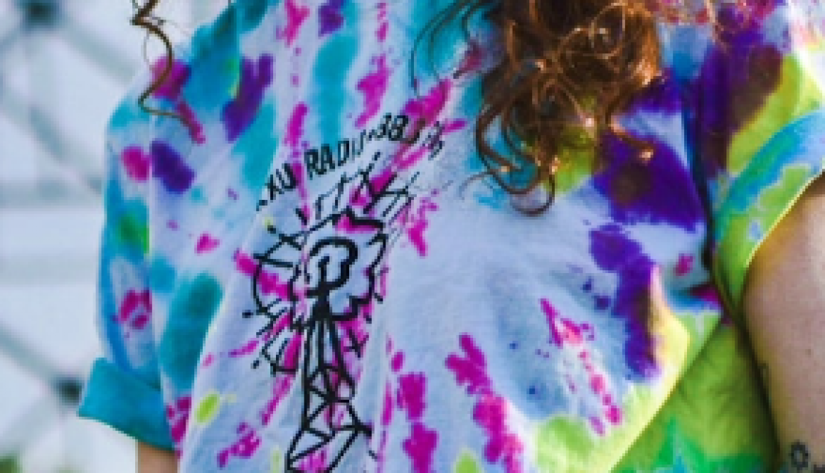 Pictured is a woman with long curly brown hair laughing. The picture cuts off at her nose, and she is wearing a FUndrive 2021 t-shirt that is tie dyed teal, pink, purple, and yellow.